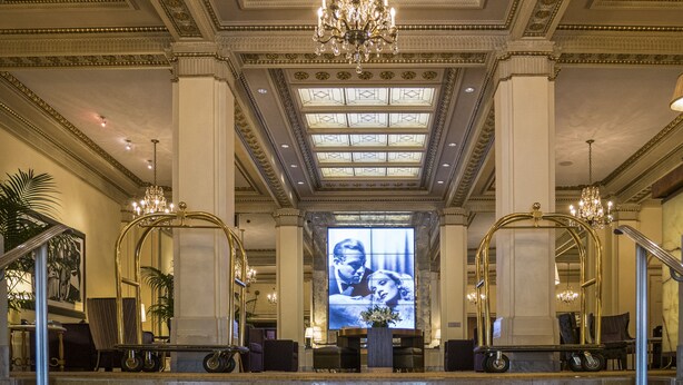 A grand lobby with a high ceiling, ornate chandeliers, and a large digital screen displaying an image.