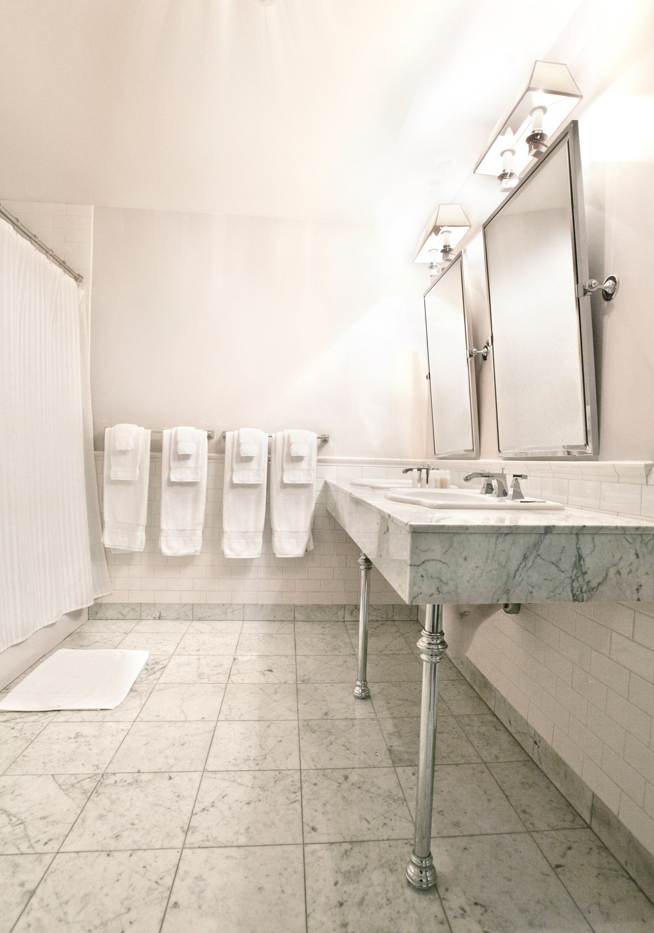 A bathroom with a marble sink, two mirrors, and a towel rack with multiple towels.