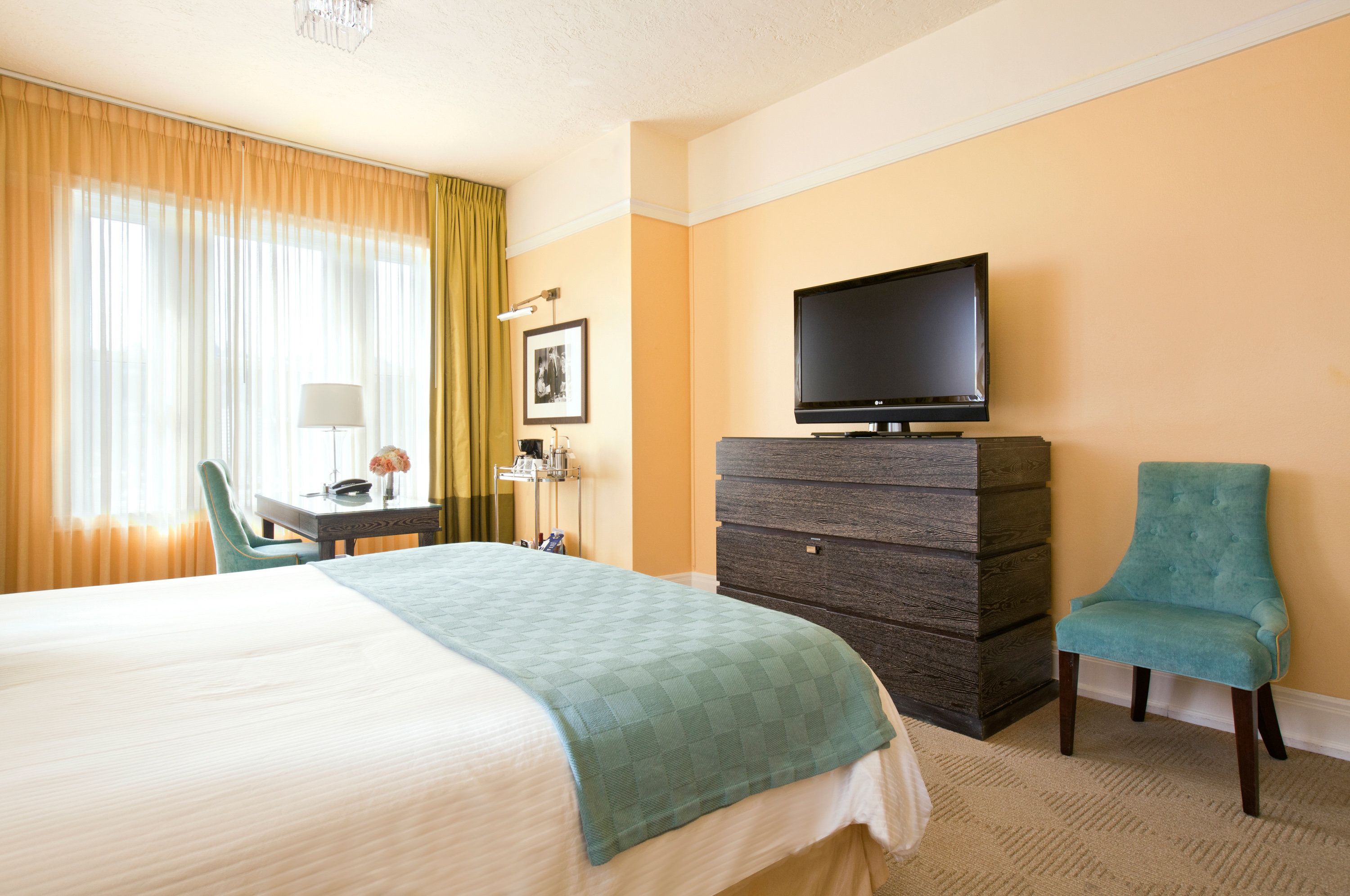 Una habitación de hotel con cama, escritorio, televisor, cómoda y una silla.