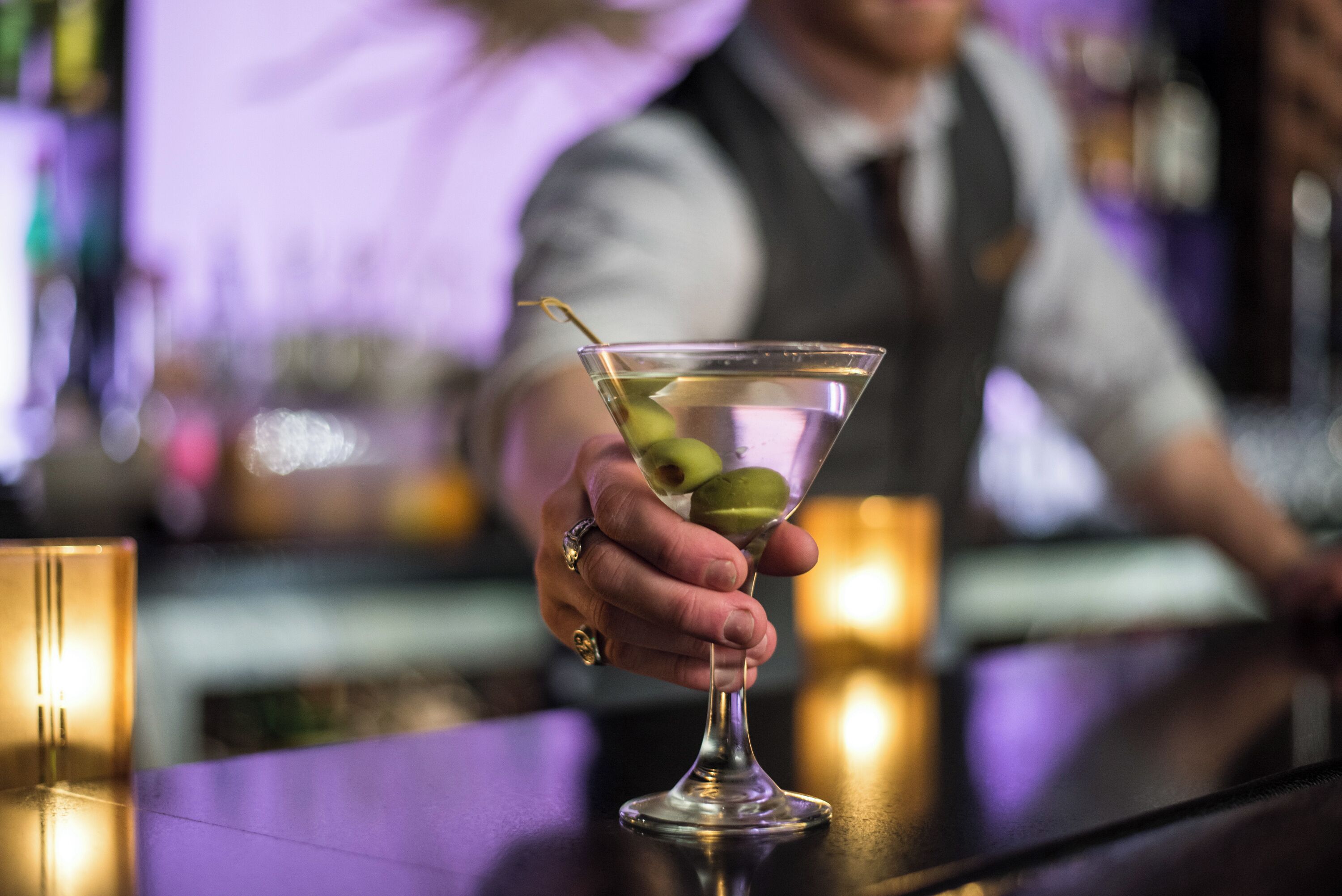 A martini glass with olives on a bar counter.