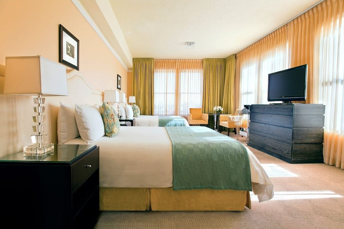 Habitación de hotel con dos camas, televisión, cómoda y escritorio con lámpara.