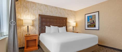 Une chambre d’hôtel avec un grand lit, deux tables de chevet avec des lampes, un mur décoré d’un motif et un tableau encadré accroché au mur.