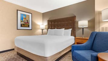 A hotel room with a large bed, two bedside lamps, a framed picture on the wall, and a blue armchair.