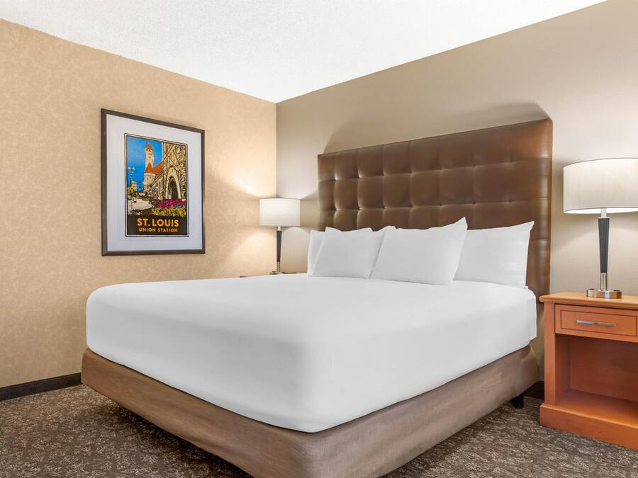 A hotel room with a large bed, two bedside lamps, a framed picture on the wall, and a wooden nightstand.