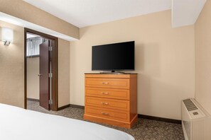 A hotel room with a bed, a wooden dresser with drawers, a television on top, and a door leading to another room. - Drury Plaza Hotel St. Louis Union Station (St. Louis)