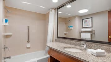 Un baño con una bañera, dos lavamanos, un tocador, una ducha con barra de apoyo y un espejo grande.