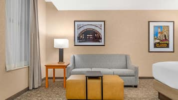 A hotel room with a sofa, a small table with a lamp, a bed, and two framed pictures on the wall.