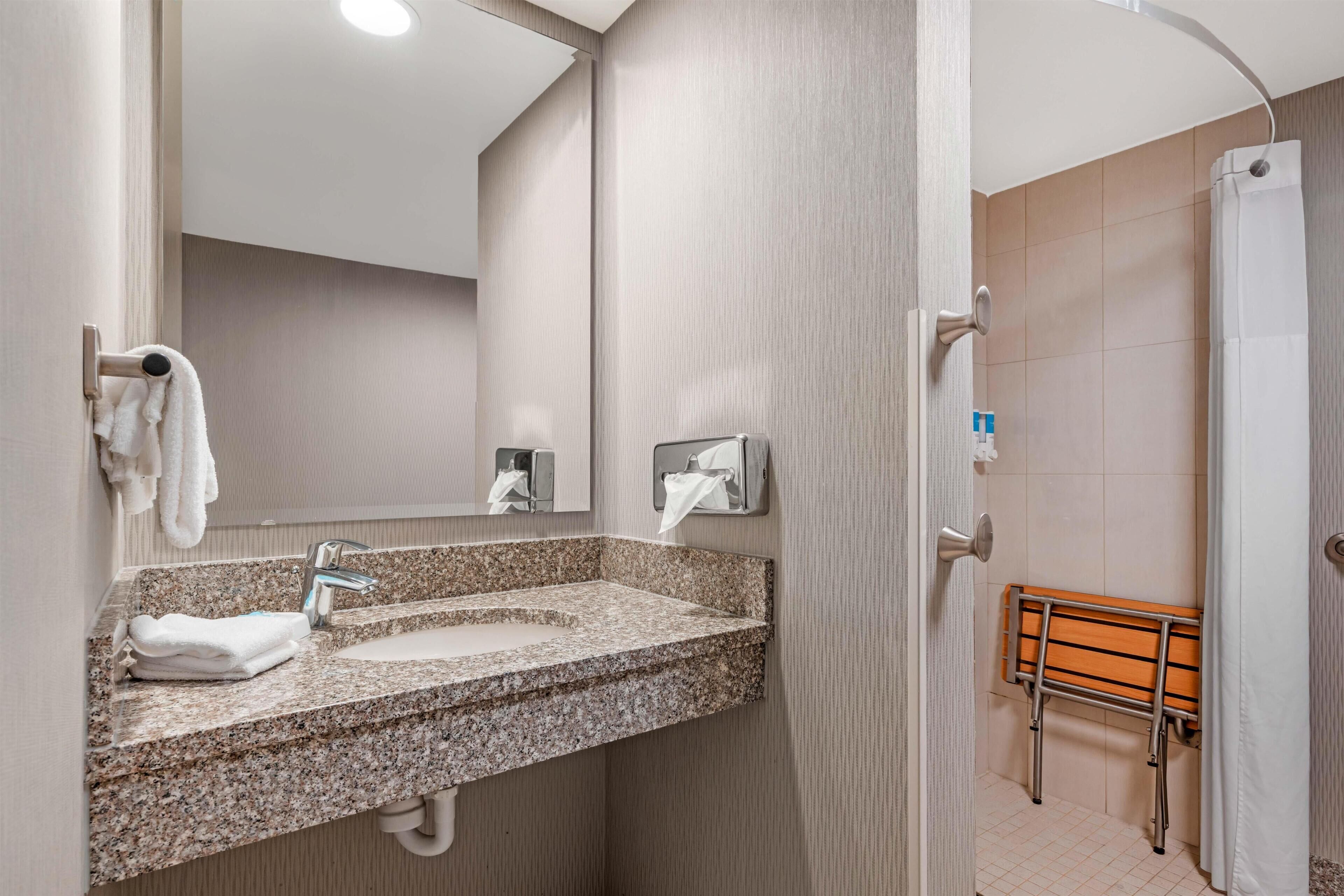 Baño con lavamanos de granito, toallero y zona de ducha con banco de madera.