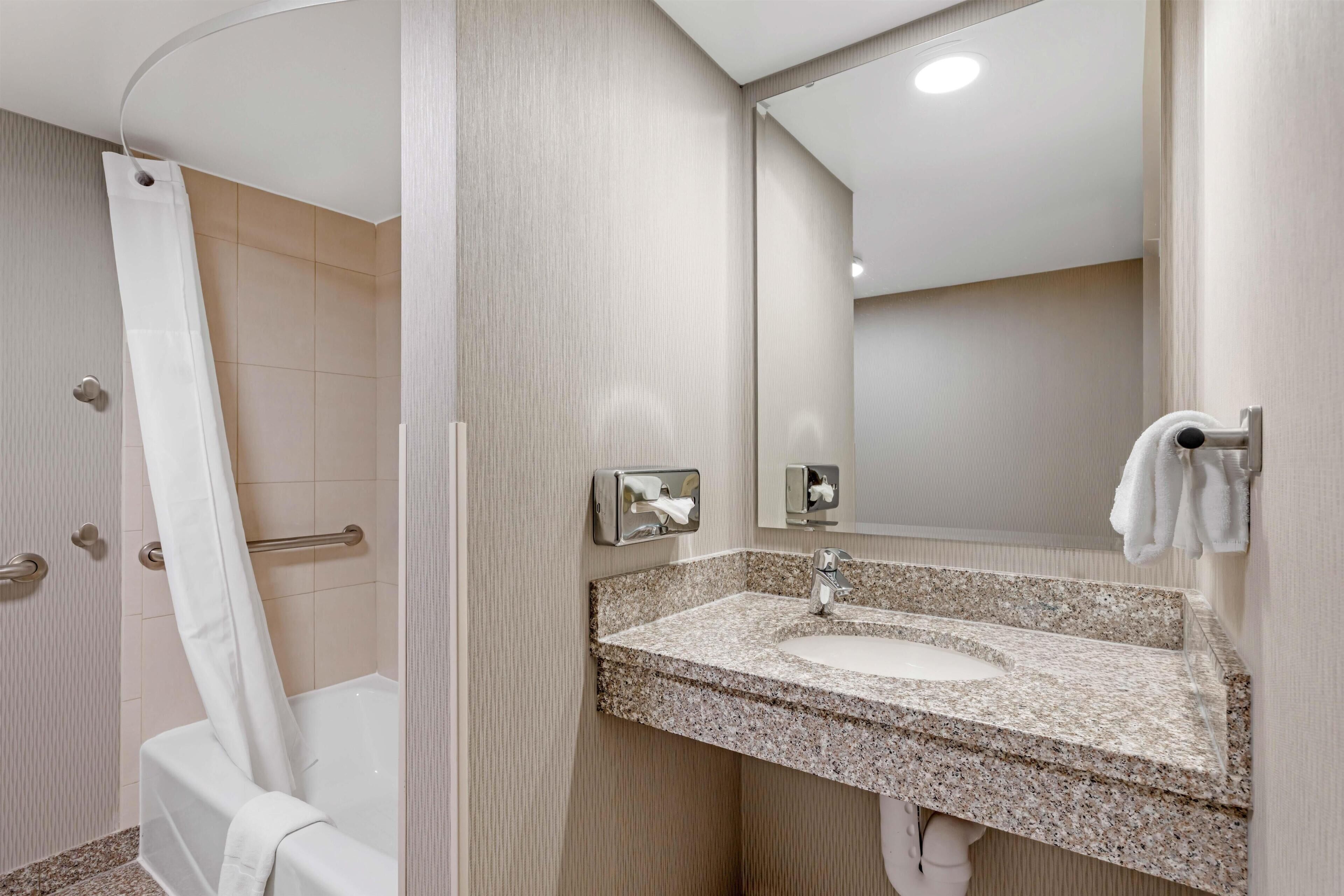 A modern bathroom with a shower, a sink with a granite countertop, and a mirror.