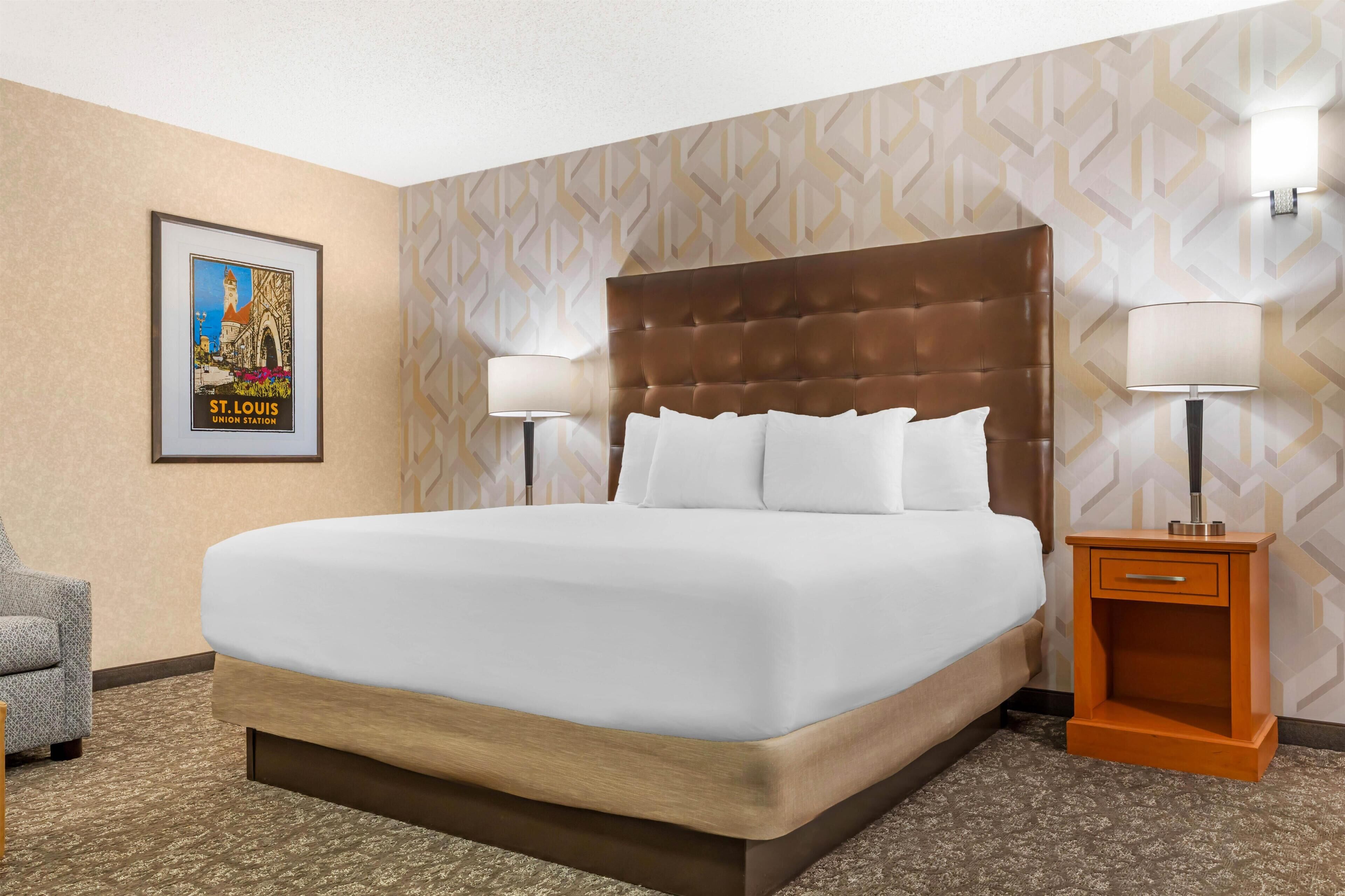 Habitación de hotel con una cama grande, dos lámparas de noche, un cuadro en la pared y una mesita de noche de madera.