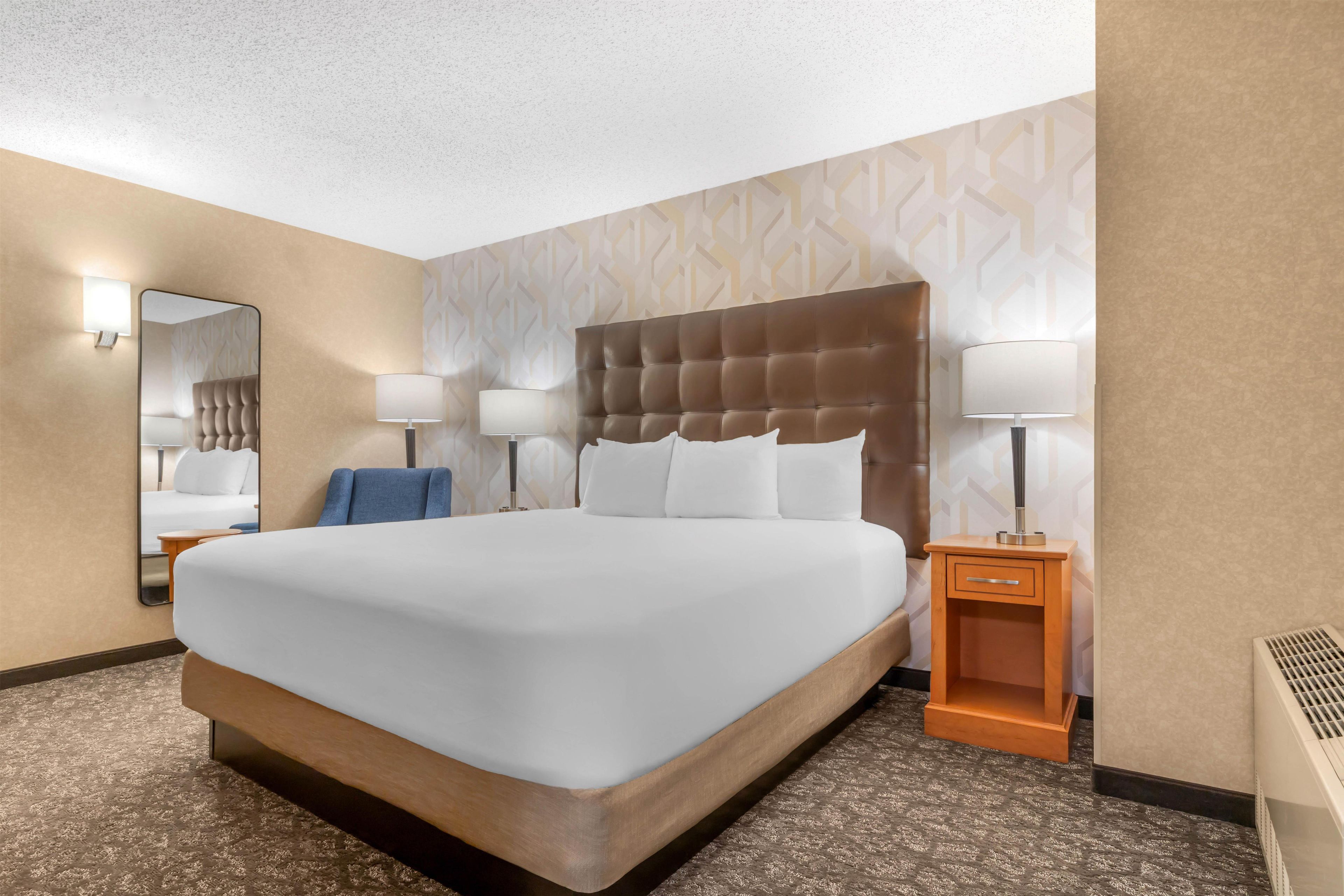 A hotel room with a large bed, two bedside lamps, a nightstand, a mirror, and a patterned wall.