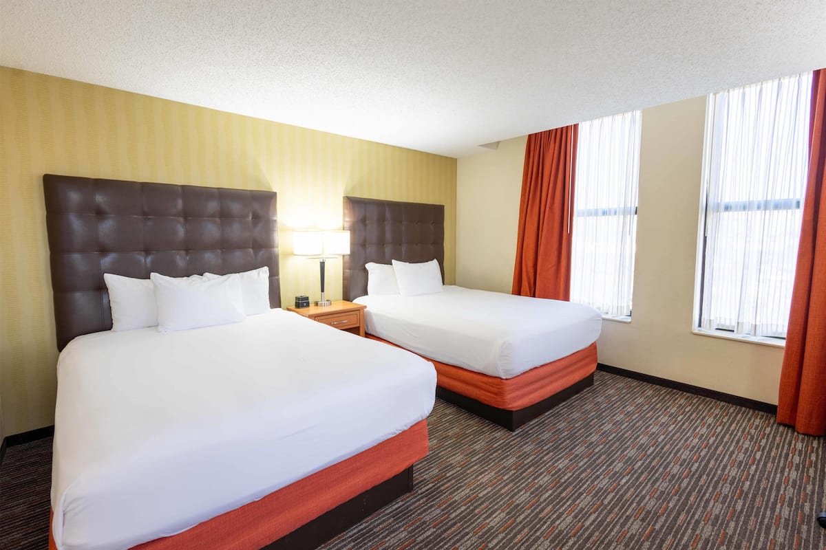 A hotel room with two beds, a nightstand, a lamp, and a window with curtains.