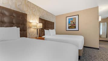 A hotel room with two beds, a headboard, a nightstand with lamps, a framed picture on the wall, and a carpeted floor.