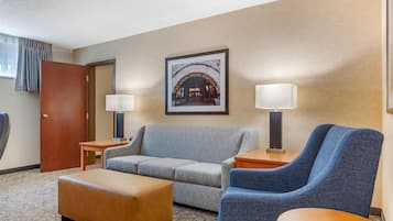 A hotel room with a sofa, ottoman, two side tables with lamps, a door, and a framed picture on the wall.