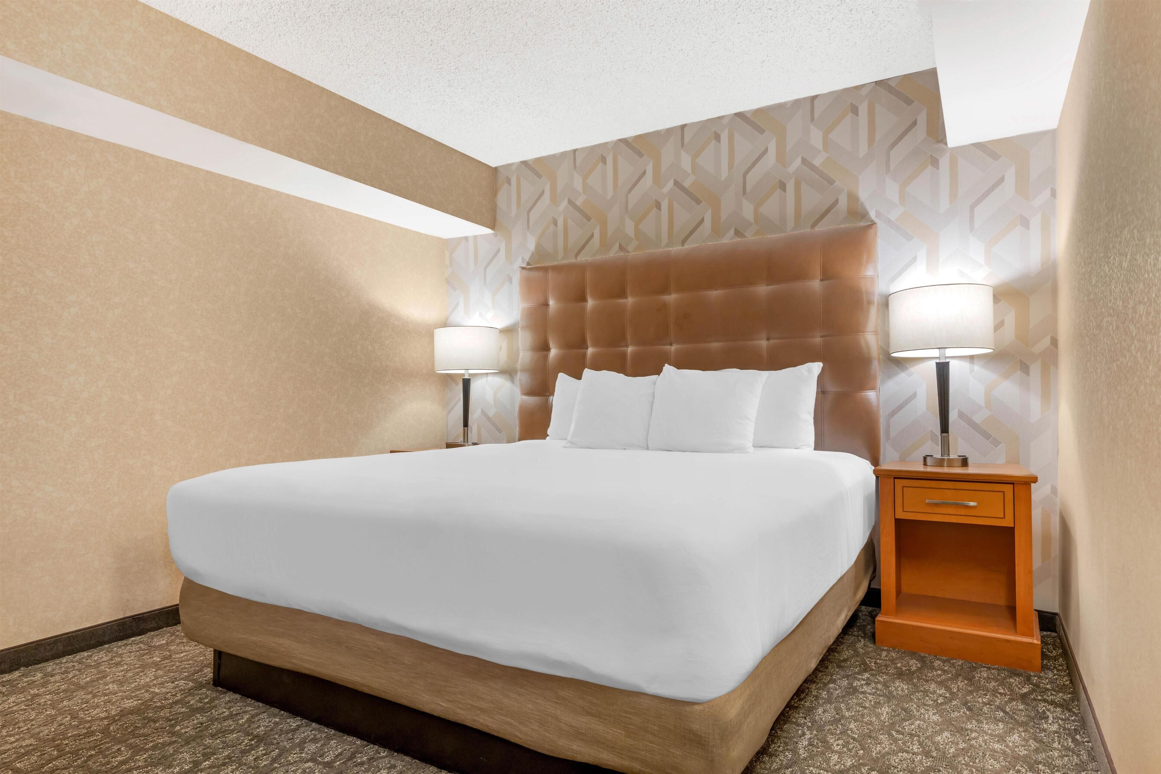 A hotel room with a large bed, two bedside lamps, a wooden nightstand, and patterned wallpaper.