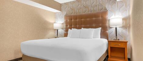 A hotel room with a large bed, two bedside lamps, a wooden nightstand, and patterned wallpaper.
