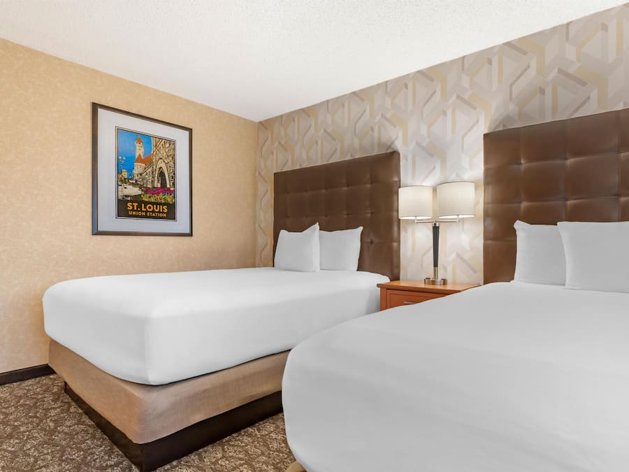 A hotel room with two beds, a framed picture on the wall, and a patterned wallpaper.