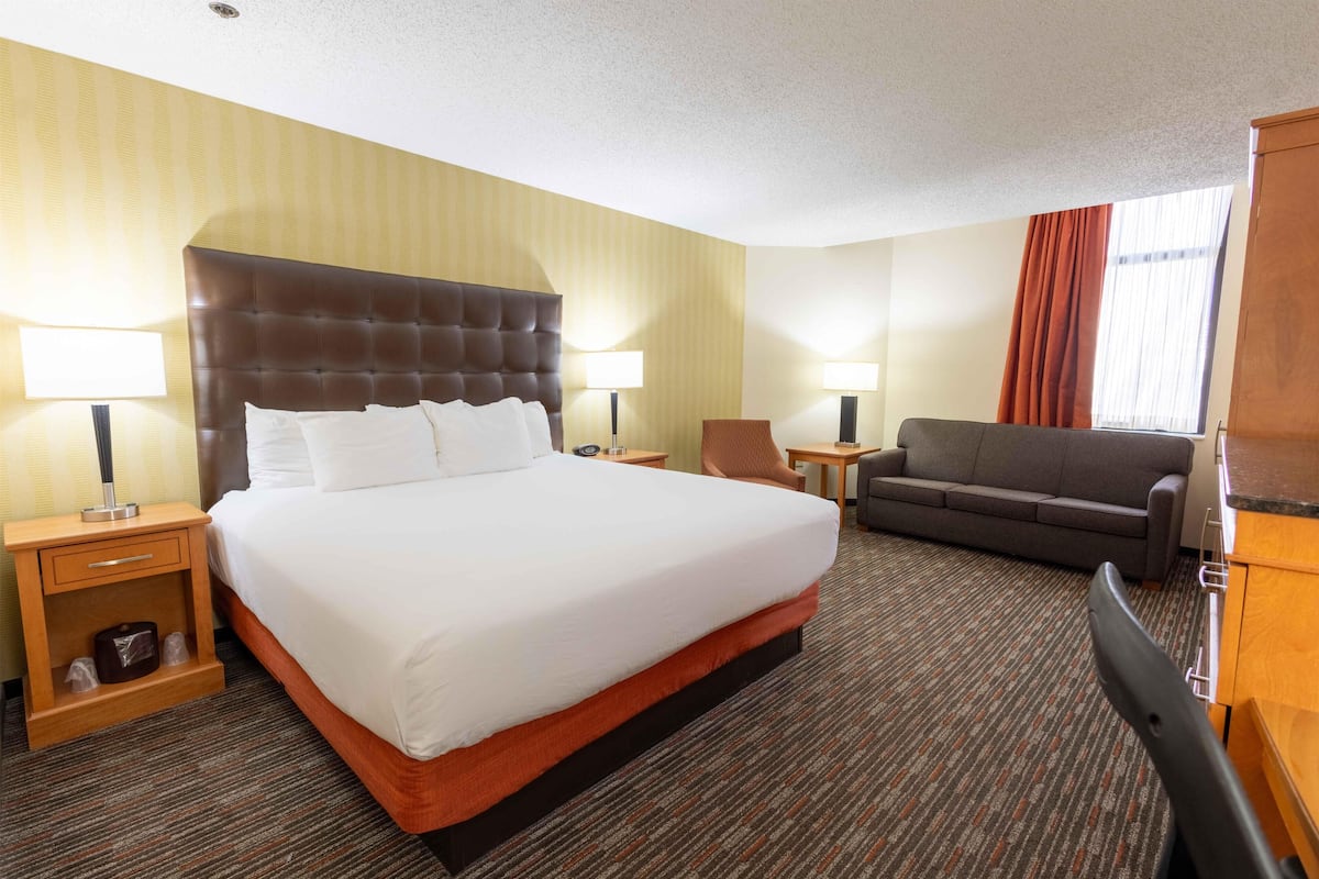 A hotel room with a large bed, two bedside tables, a sofa, a desk, and a chair.