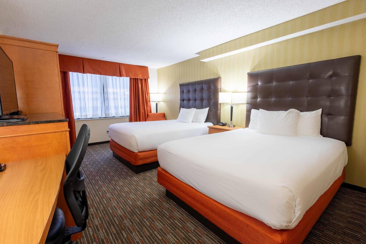 A hotel room with two beds, a desk, a chair, and a window with curtains.