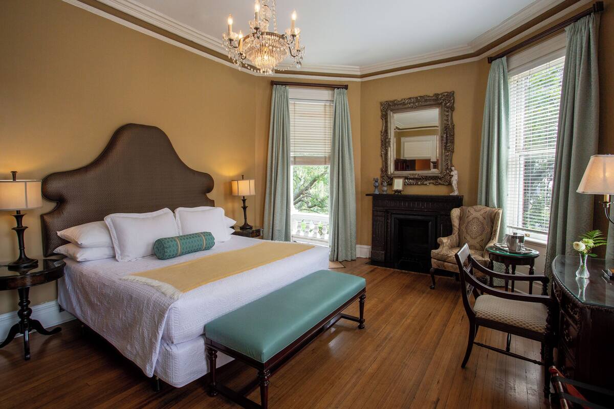 A spacious bedroom with a large bed, a bench, a fireplace, and a chair.