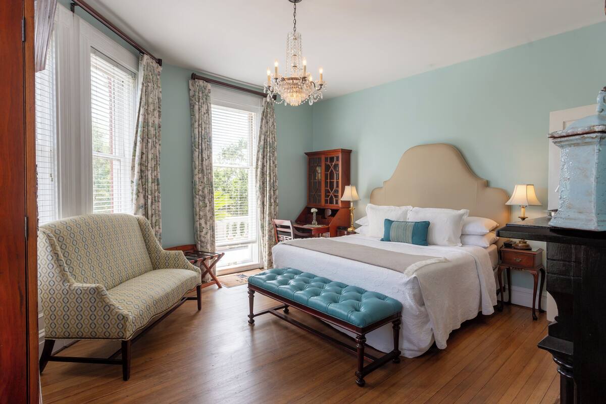 A bedroom with a large bed, a bench, a chair, a dresser, and a chandelier.