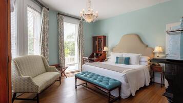 A bedroom with a large bed, a bench, a chair, a dresser, and a chandelier.