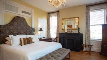 A bedroom with a large bed, a bench, a fireplace, a mirror, and a chandelier.