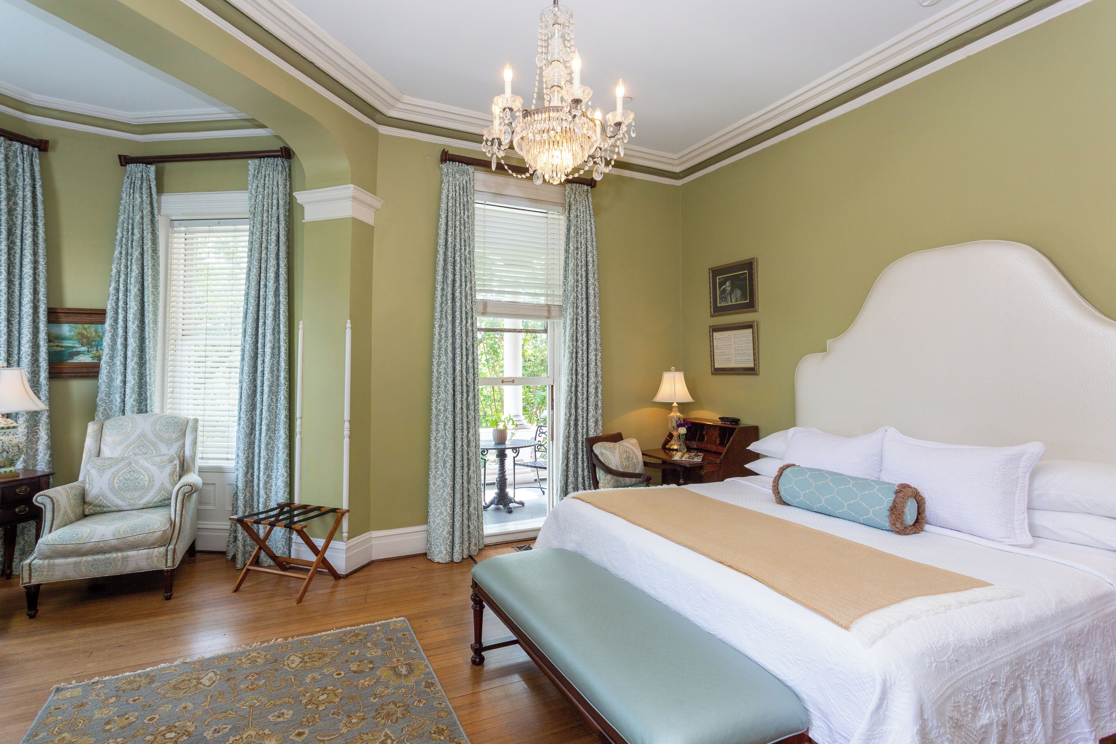 A bedroom with a large bed, a chandelier, a chair, and a view of the outdoors.