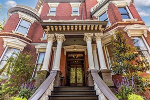 A grand entrance with a central door flanked by columns, a staircase leading up, and a well-maintained garden with various plants. - Kehoe House, Historic Inns of Savannah (Savannah)