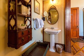 A bathroom with a wooden vanity, a white pedestal sink, a mirror, and a wooden door.