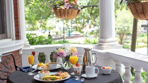A breakfast table set with various dishes, a pitcher, and a vase of flowers on a balcony with a view of greenery. - Kehoe House, Historic Inns of Savannah (Savannah)
