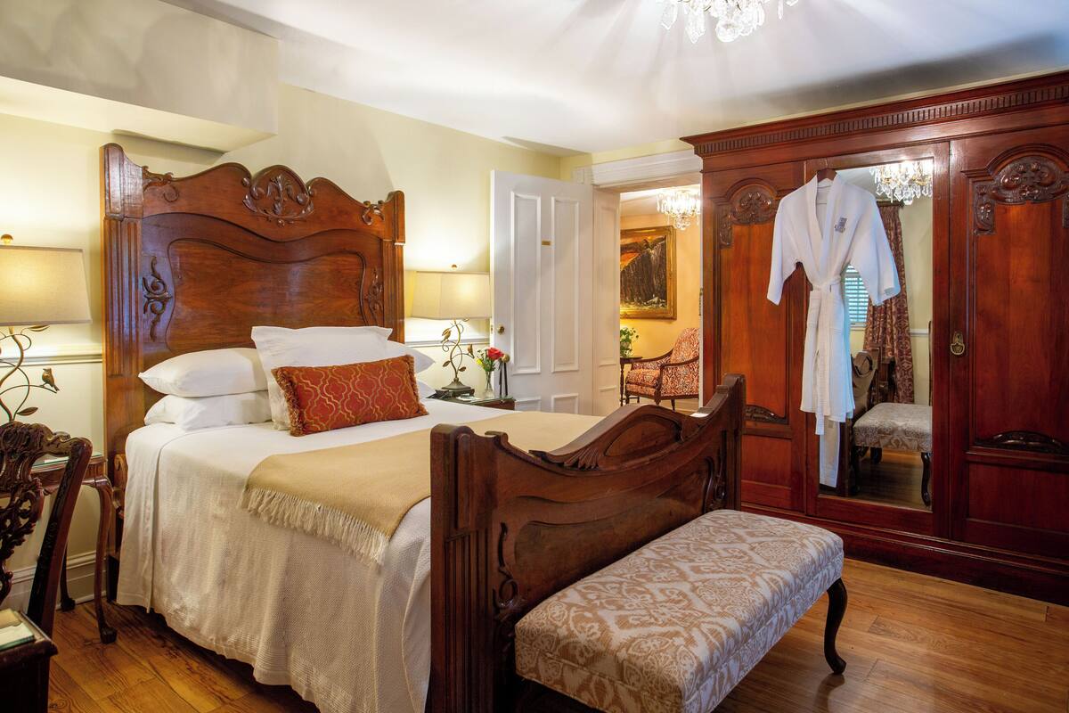 A bedroom with a large bed, a wooden headboard, a bench, a mirror, and a wardrobe.
