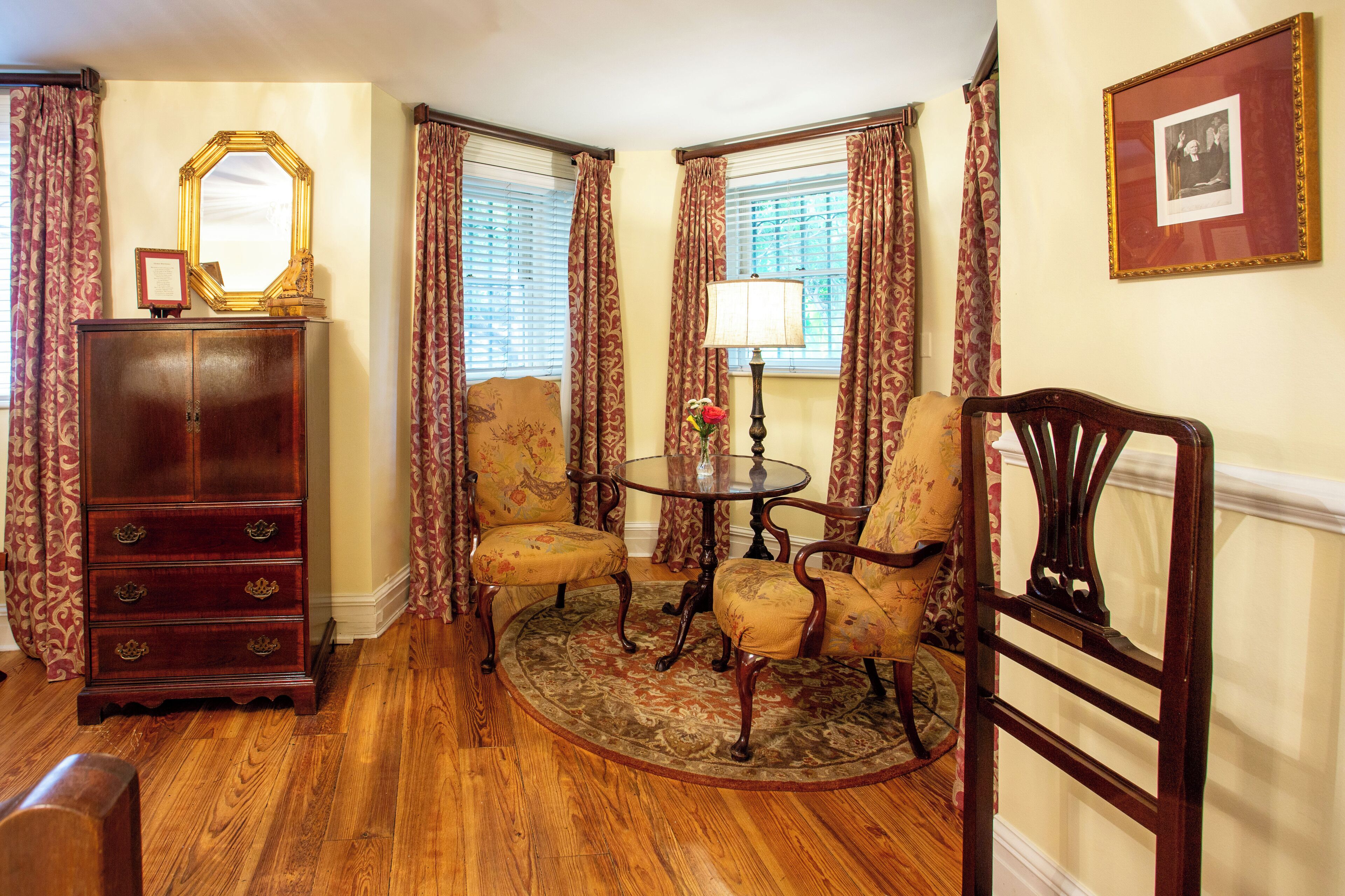 A room with a wooden floor, a round table with chairs, a dresser, and a mirror on the wall.