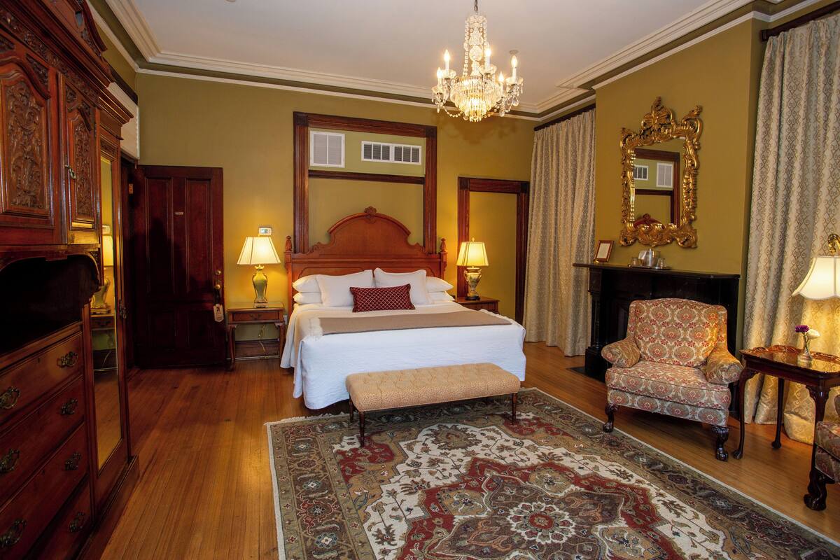 A well-appointed bedroom with a large bed, a bench, a chair, a dresser, a mirror, and a chandelier.