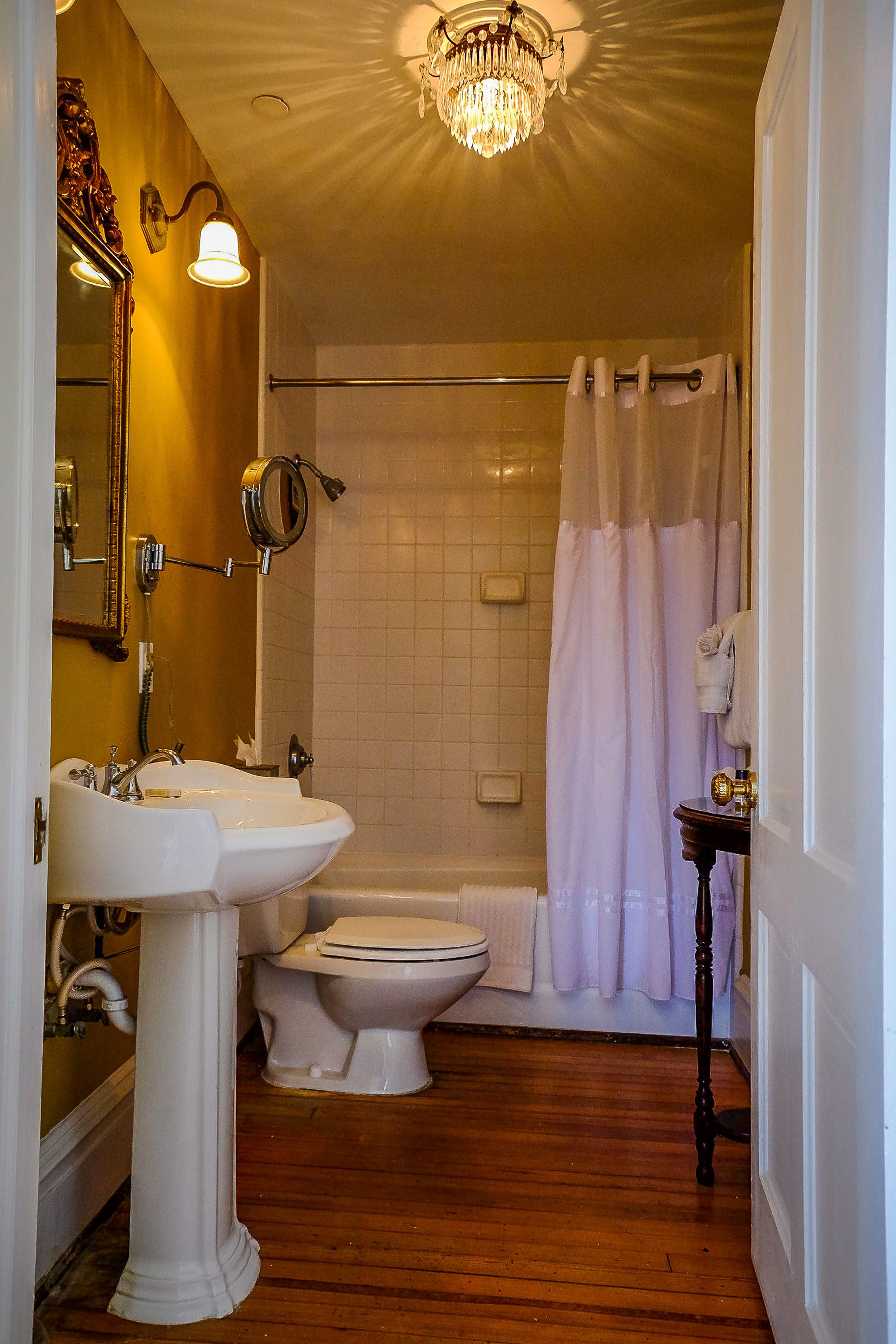 A bathroom with a pedestal sink, toilet, and shower area with a curtain.