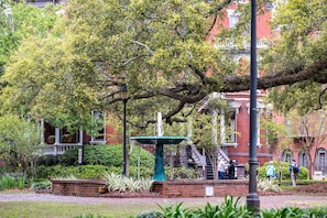 A brick building with a large tree in front, a fountain, and a brick pathway.