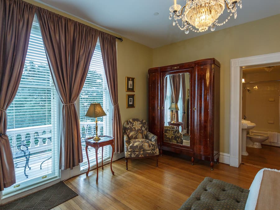 A living room with a wooden floor, a large armchair, a small table with a lamp, and a mirror cabinet.