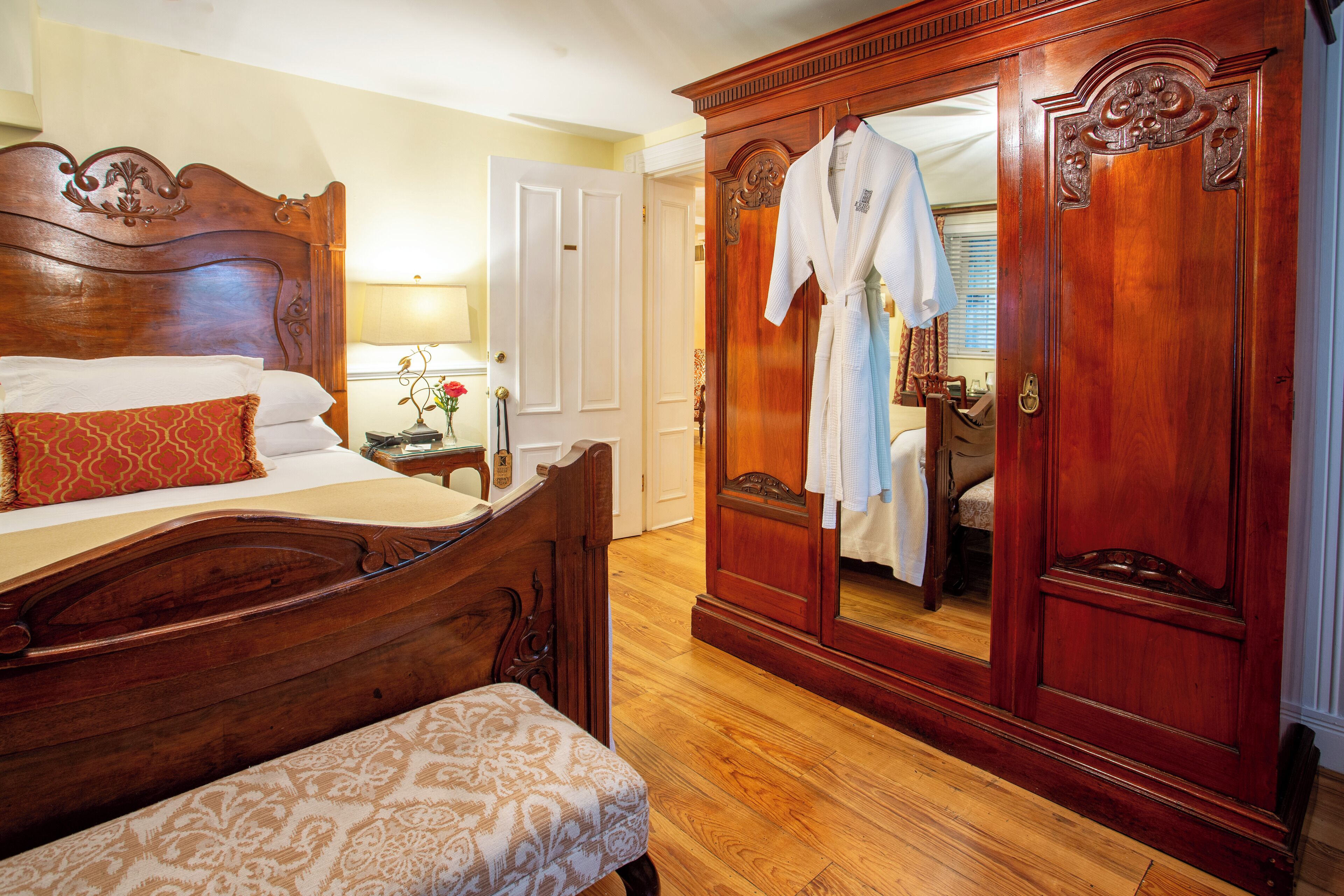A bedroom with a wooden bed, a bench, a wardrobe, and a mirror.