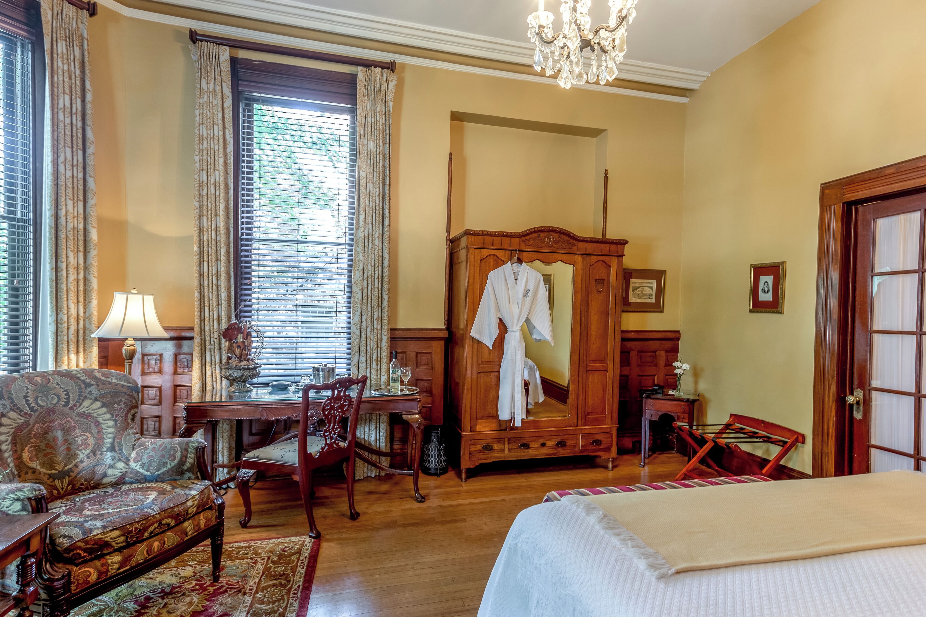 Une pièce comprenant un lit, une armoire en bois, un bureau avec une lampe, une chaise et une fenêtre avec des rideaux.
