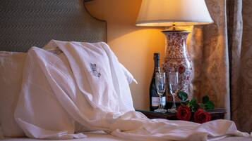 A hotel room with a bed, a white robe, a bottle of champagne, two wine glasses, and a vase with red roses.