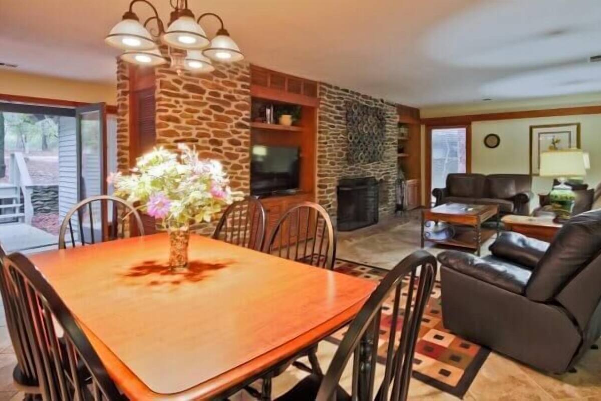 A dining area with a wooden table and chairs, a stone fireplace, and a living room with a leather sofa and a television.
