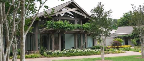Un edificio moderno con techo inclinado, ventanas amplias y un jardín bien cuidado con diversas plantas y flores.