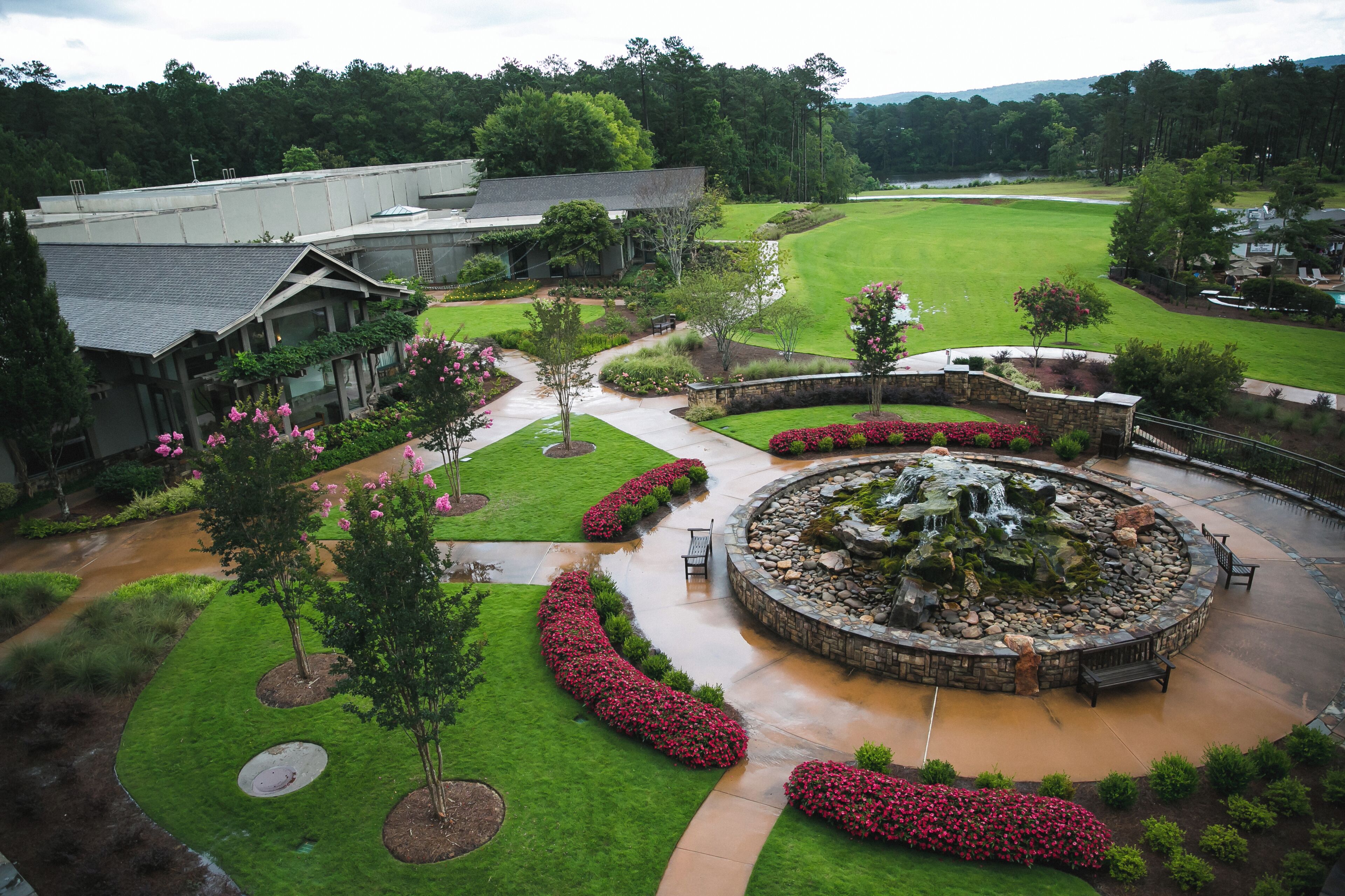 A landscaped courtyard with a circular water feature, a pathway, and a building with a sloped roof.