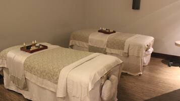 A room with two beds covered in white linens, a tray with candles, and a wooden floor.