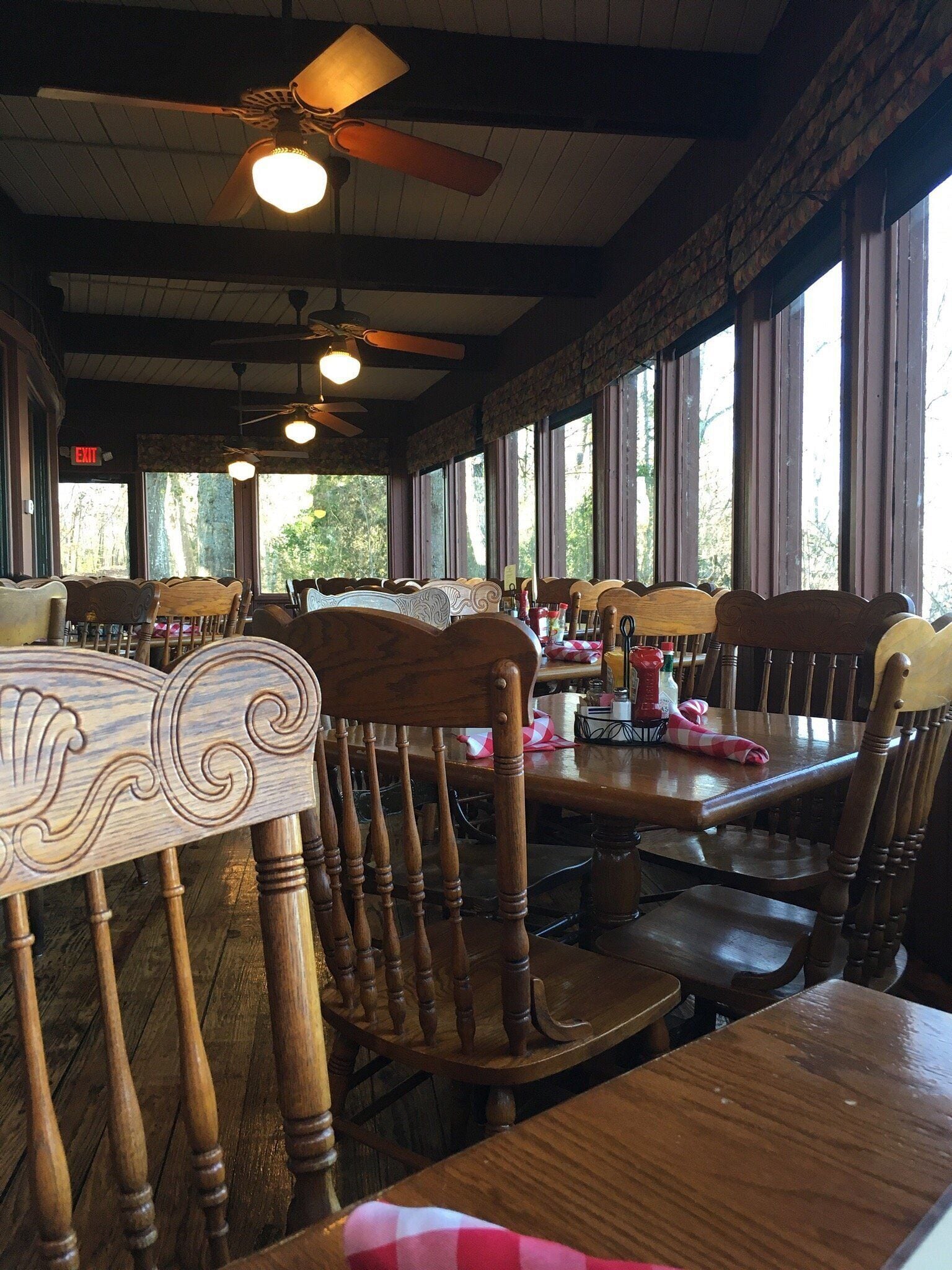 A restaurant interior with wooden chairs, tables, ceiling fans, and large windows.