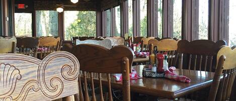 Un interior de restaurante con sillas y mesas de madera, ventiladores de techo y ventanas amplias.