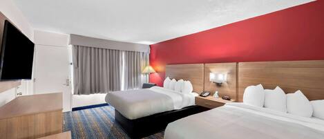 A hotel room with two beds, a desk, a TV, and a red accent wall.