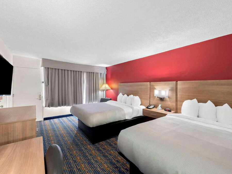 A hotel room with two beds, a desk, a TV, and a red accent wall.
