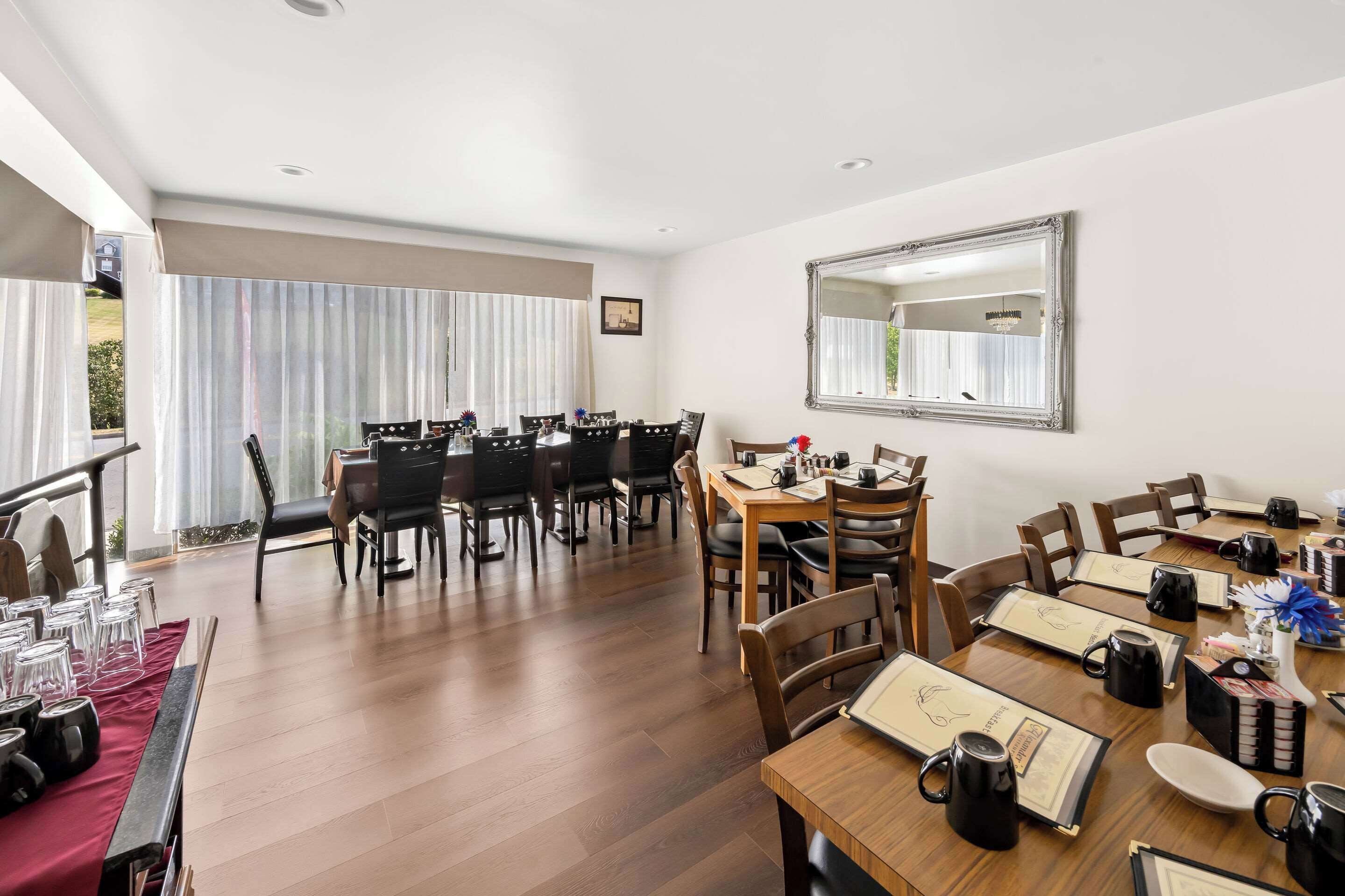 A dining area with multiple tables and chairs, a large mirror on the wall, and a view of the outdoors through large windows.