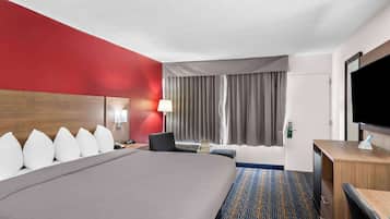 A hotel room with a large bed, a desk, a chair, a TV, and a window with curtains.